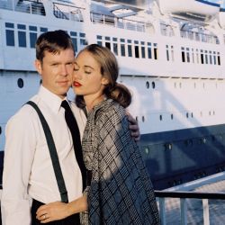 A beautiful woman leans in and hugs a handsome man next to a cruise ship