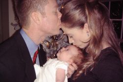 A loving husband kisses his wife's forehead as she kisses the baby they're holding
