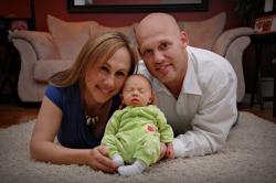 Beautiful parents proudly hold their sleeping baby while lying on a rug