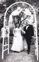 Beautiful archway frames this black and white photo of a married couple walking hand in hand