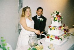 A bride laughs as her husband helps her cut the wedding cake