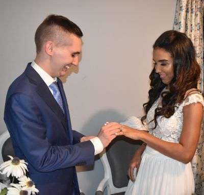 Ecstatic groom putting wedding ring on beautiful Christian bride