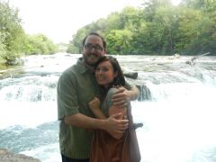 A couple hug tightly in front rapids in the summertime