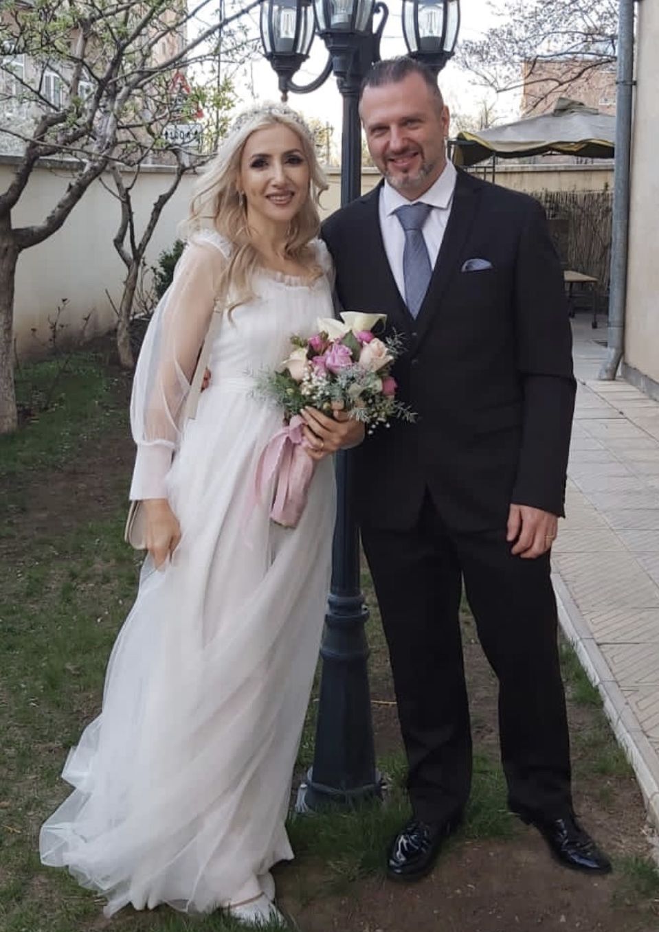 A beautiful blonde bride holds flowers as she stands next to her new Christian husband, as they celebrate outdoors