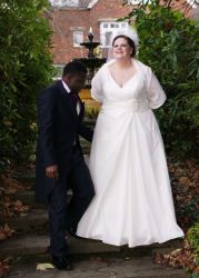 A groom ensures his new wife is comfortable outdoors while she leans near a fountain