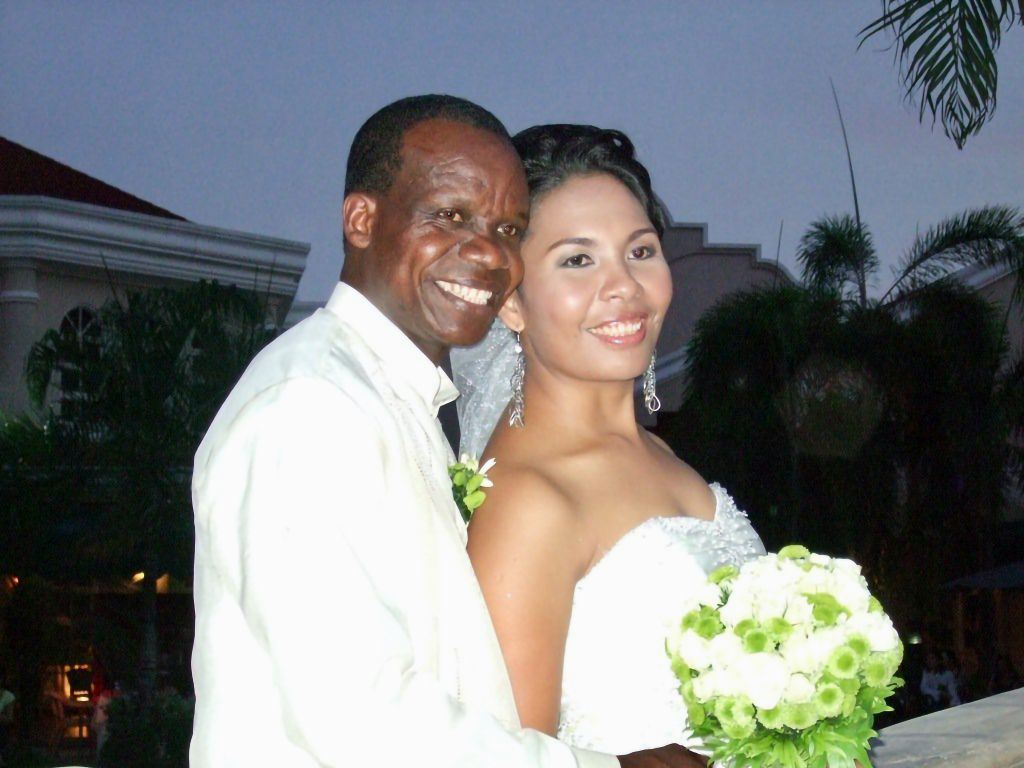 A proud Black Christian man smiles while holding his new Asian bride