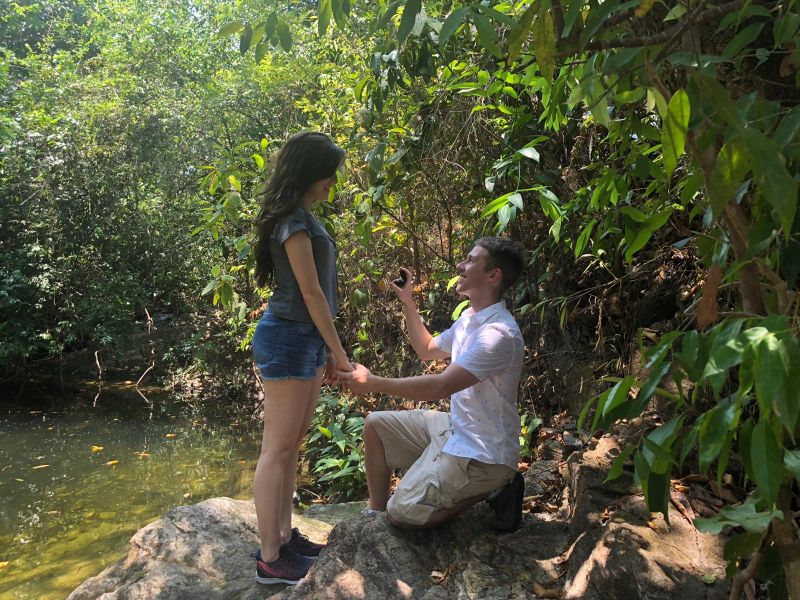 A single Christian man proposes near a stream while on bended knee