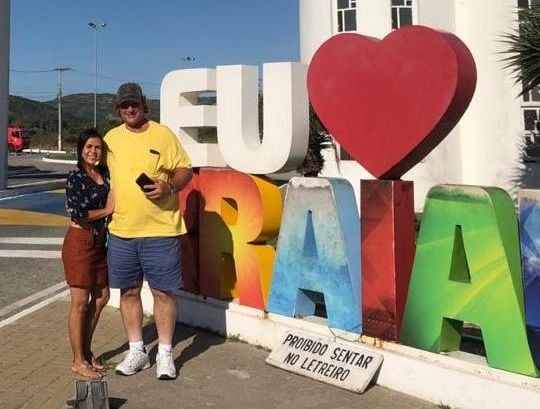 A man in a yellow shirt and blue shorts stands next to a woman in a flowery top and maroon shorts on a windy day in Arraial do Cabo, Brazil