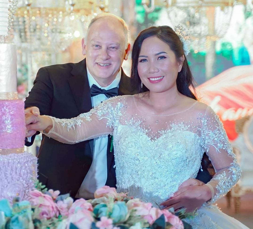 A beautiful Asian Christian woman and her Caucasian husband cut the wedding cake