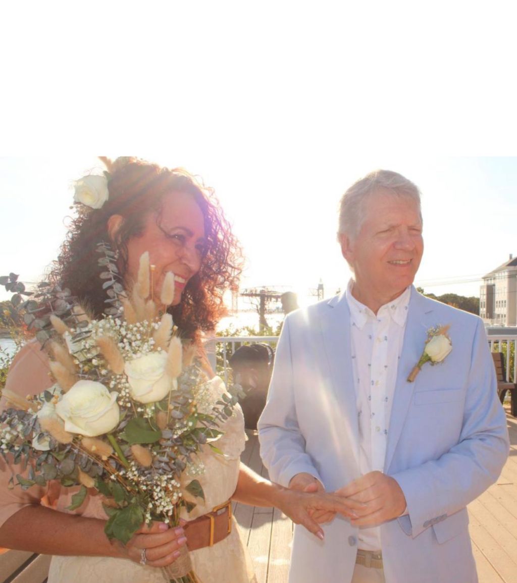 A bride smiles happily as her husband puts the wedding ring on her finger