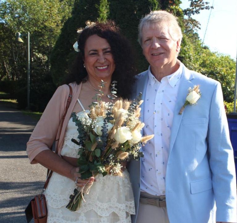 A woman poses with beautiful flowers outdoors, while holding tightly to her new husband