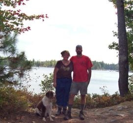 A smiling Christian couple and their dog pose on the 100 mile wilderness trail
