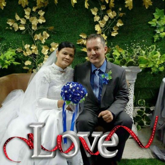 Wedded bliss for Interracial couple who are seated as bride holds blue bouquet of flowers