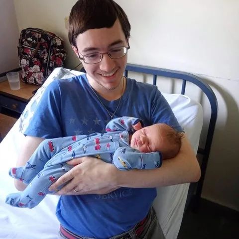 A new father beams with joy as he holds his newborn son