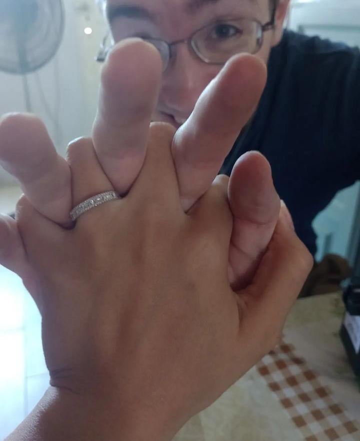 A newly engaged young Christian man holds up his fiancee's hand to the camera which shows off her engagement ring, while he peers between her fingers and laughs