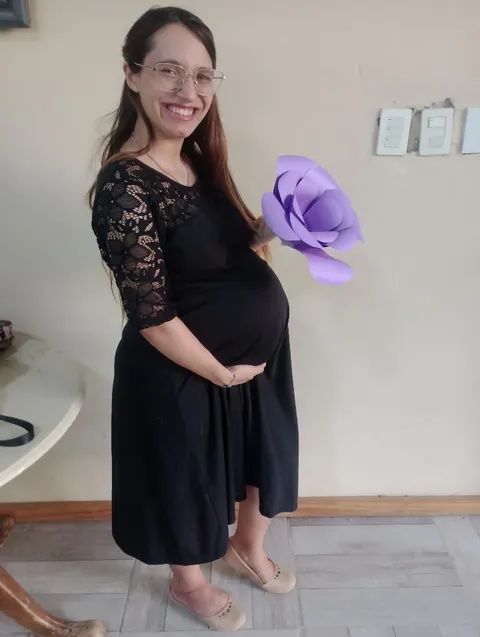 A visibly pregnant Christian woman stands in a black dress and smiles while holding her belly