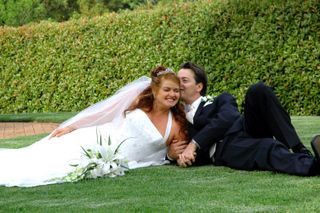 Groom whispers in his wife's ear as they lie on the grass for a photo
