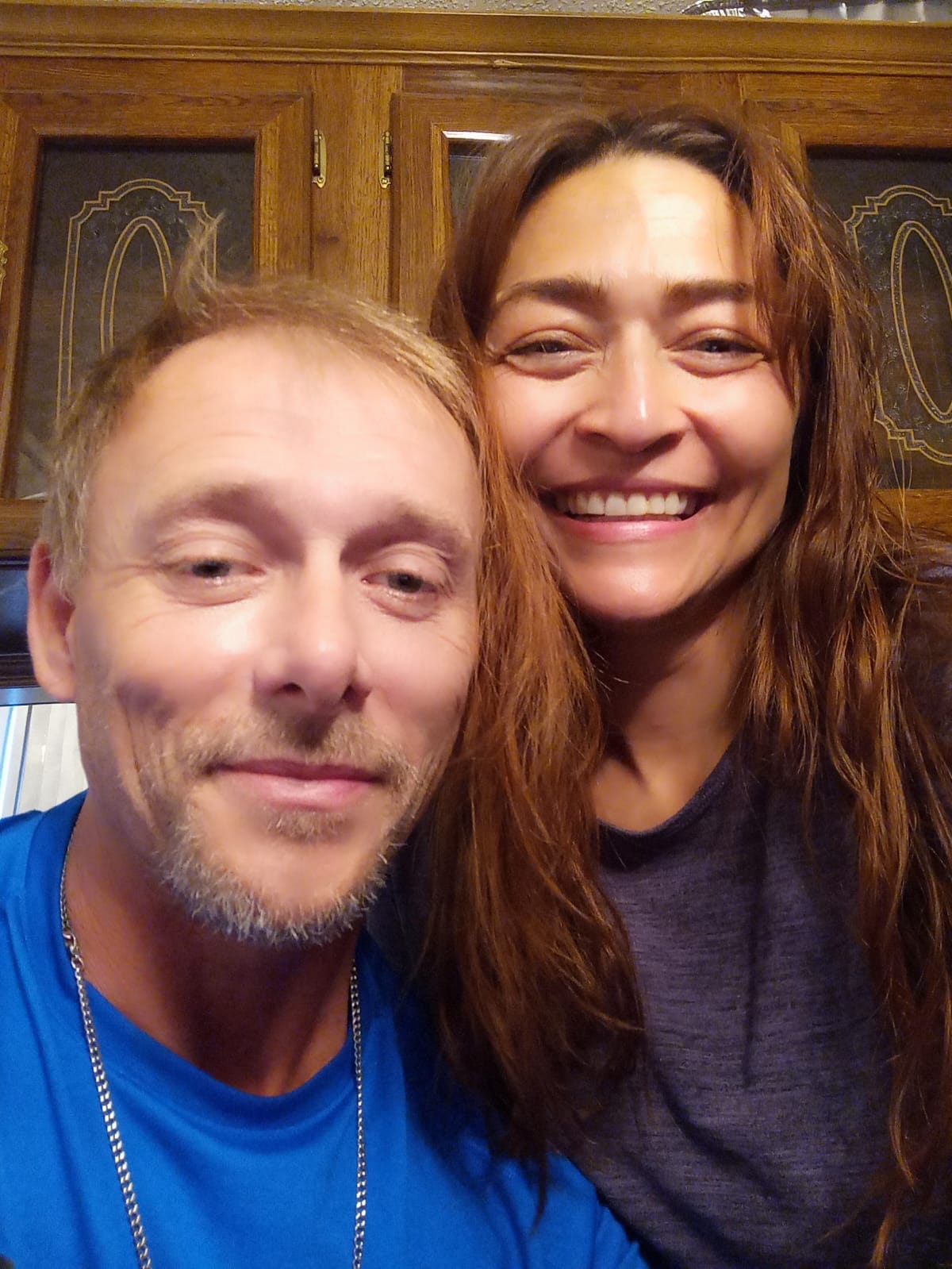 A pretty Latina Christian woman smiles behind a bearded man taking a selfie