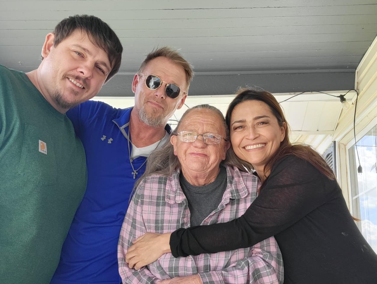 A woman hugs her in-laws on a porch outside