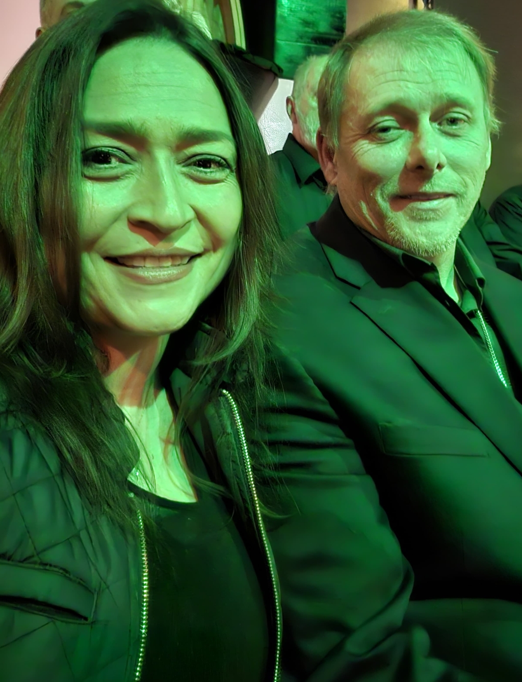 An attractive couple are bathed in a green light on a date night at a show