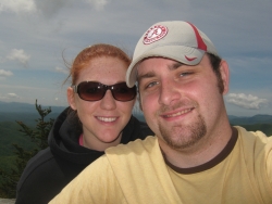 A woman in sunglasses stands behind a man in a baseball cap while on a hike