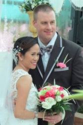 A tall man stands next to his bride who holds beautiful flowers and looks radiant in white dress