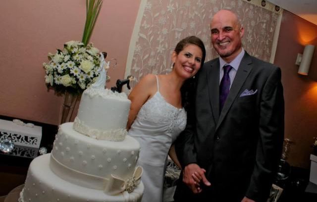 A newly wedded Christian couple laughs uncontrollably while standing behind their wedding cake