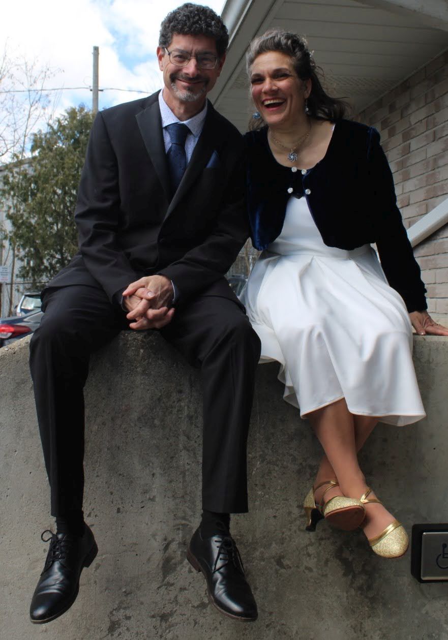 A well dressed and relaxed couple laugh while sitting on a wall
