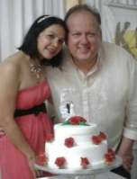 An elated man holds a rose covered wedding cake with a beautiful woman in a pink dress