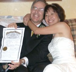 An overjoyed senior Christian woman hugs her new husband who laughs while holding up their marriage license