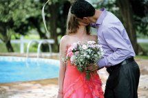 A man holds his new wife and kisses her passionately beside a pool