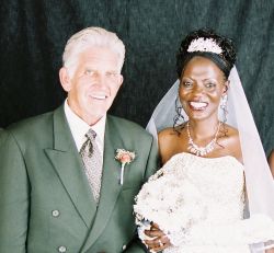 A senior Christian man stands next to his beautiful new bride, who beams with joy