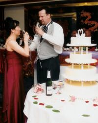 Bride and groom stand next to their wedding cake while toasting each other
