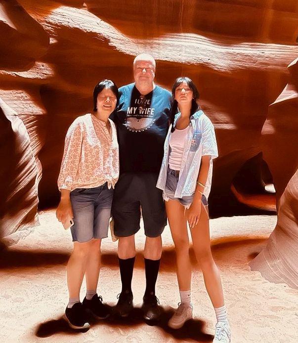 An East Asian woman stands next to a tall White Christian man, along with their daughter in front of psychedelic stones