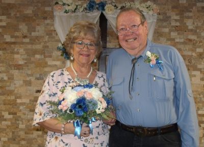 Senior Christian woman stands with bridal bouquet next to smiling husband