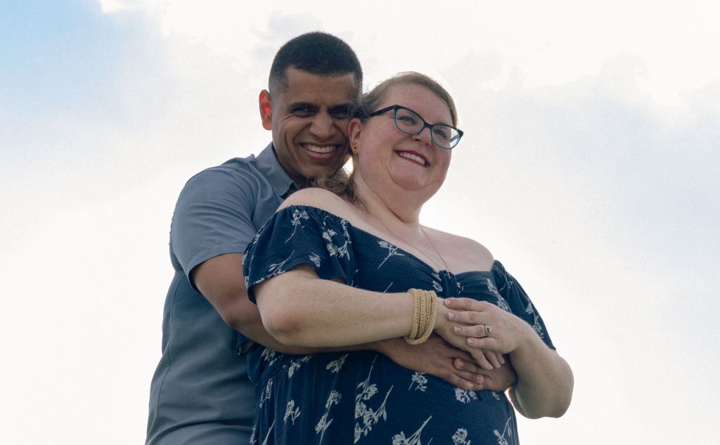 A woman smiles with joy as her husband hugs her from behind