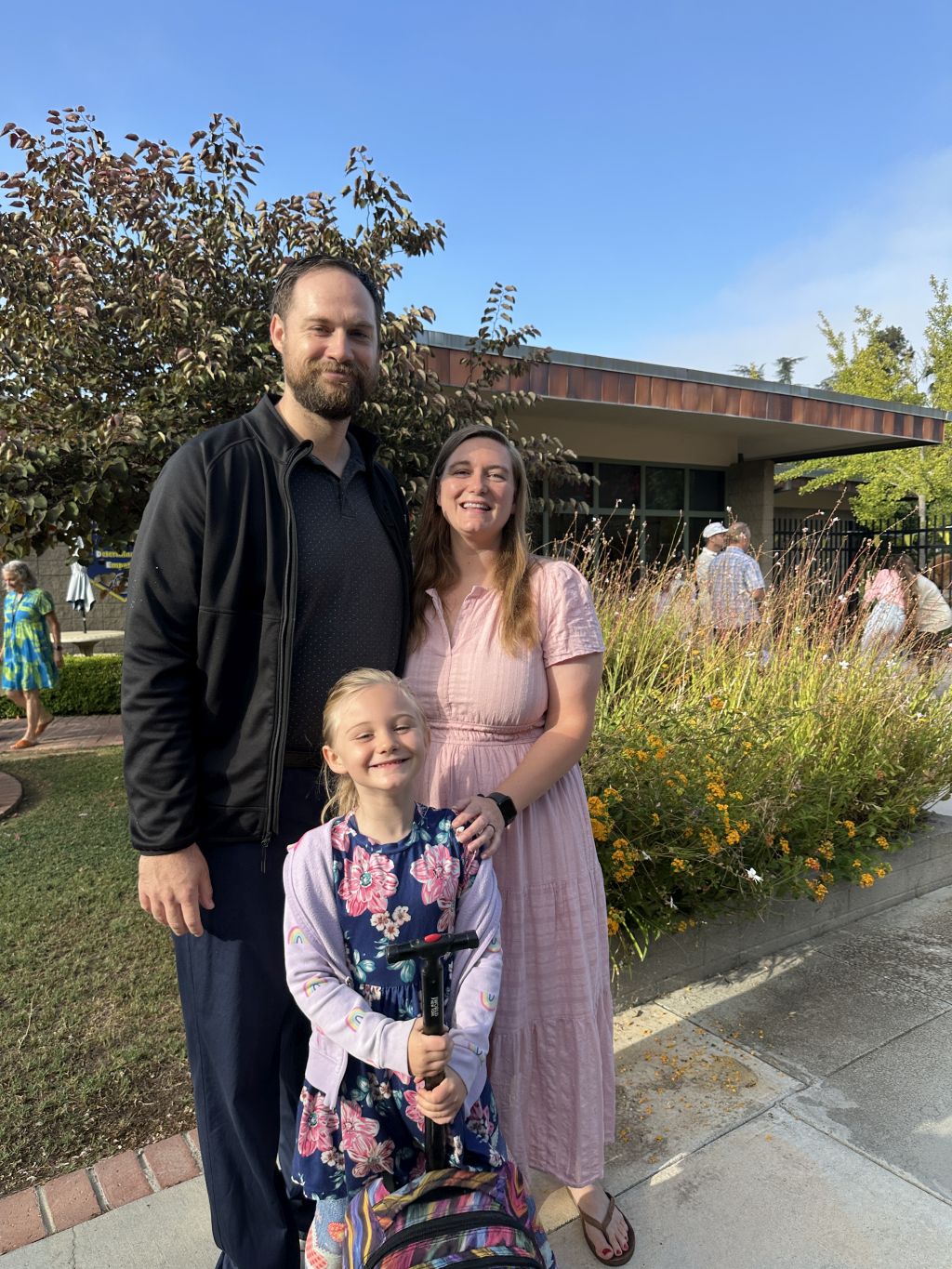 A Christian couple pose with their daughter in front of some flowers on a sunny day