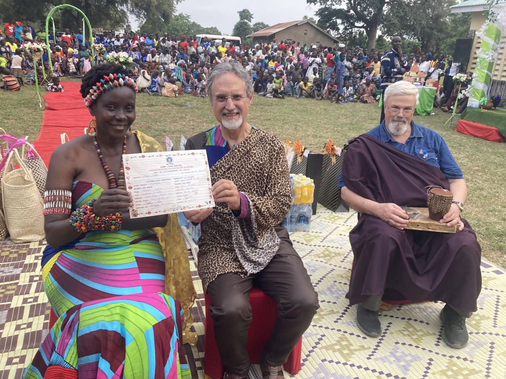 A couple in Uganda hold up proof of their wedding license while a huge crowd applauds behind them