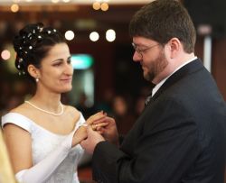 A beautiful bride looks at her new husband lovingly as he places a ring on her finger