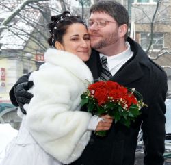 A man tenderly hugs a beautiful woman who holds flowers in a winter setting
