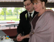 A man tenderly puts his arm around a kind looking woman as she cuts a cake
