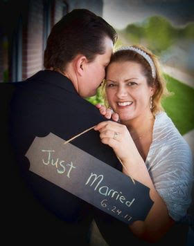Wife smiling ear to ear while hugging new husband and holding Just Married sign