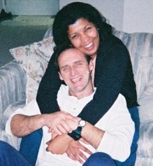 A woman laughs on the couch as she hugs a joyful man