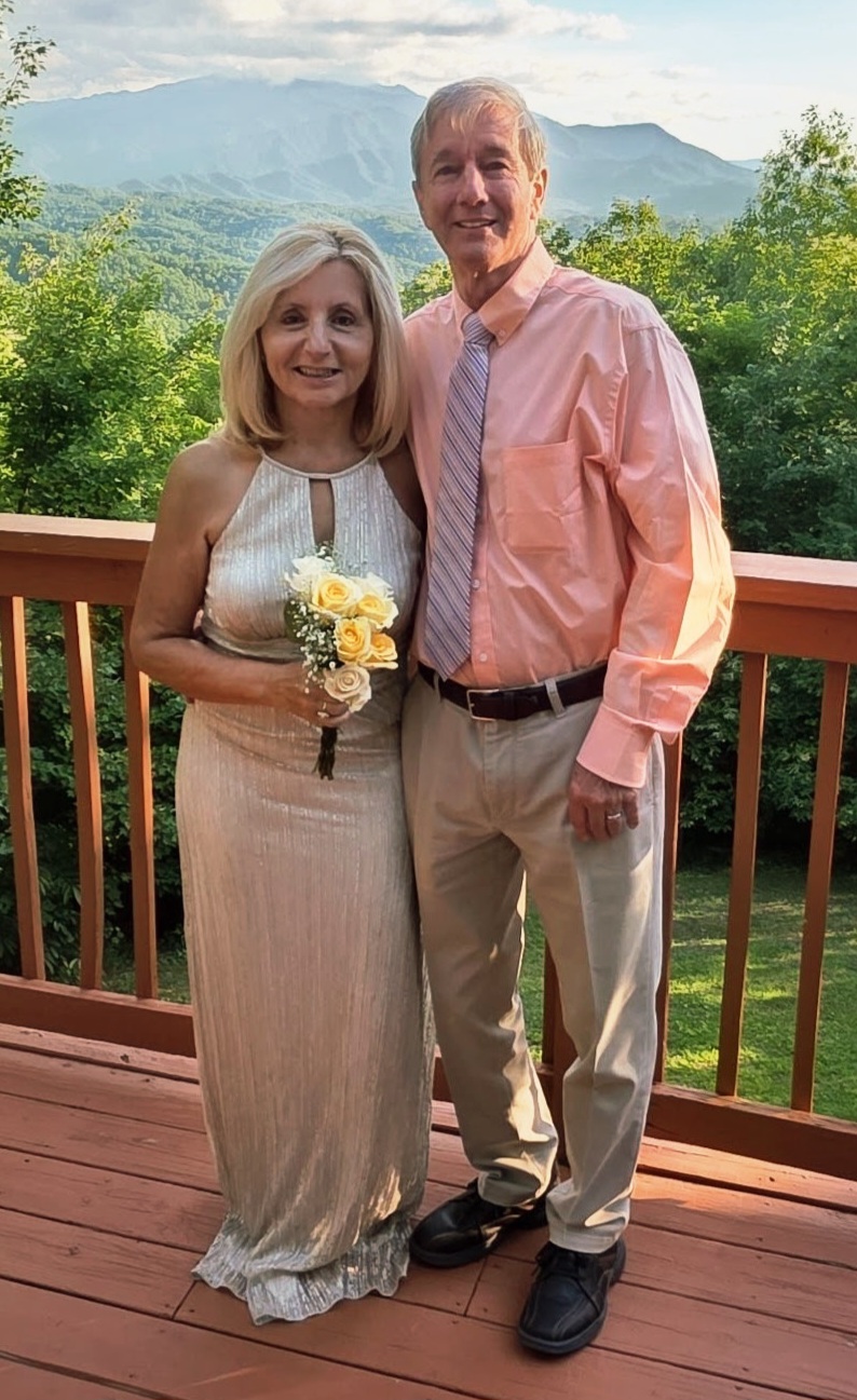 A very happy and well-dressed couple pose on a deck overlooking beautiful scenery after their wedding