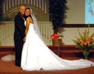 A very happy newly married Christian couple stand cheek to cheek at the altar