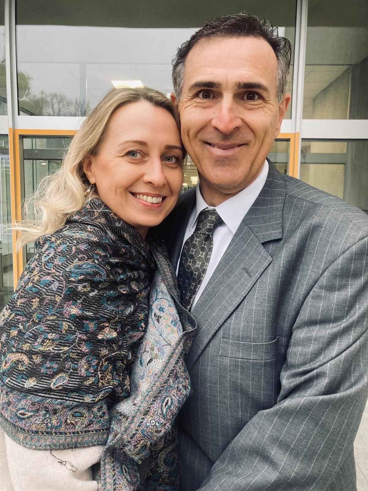 A very happy man in a suit takes a selfie while a beautiful woman leans on his shoulder and smiles