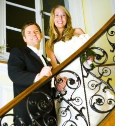 A couple stand hand in hand on a staircase and smile