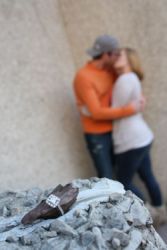An engagement ring is shown with a newly engaged couple kissing in the background