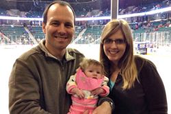 Proud parents holds their baby daughter at ice level at a hockey game