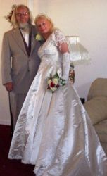 A woman in her wedding dress leans into her husband who looks very pleased